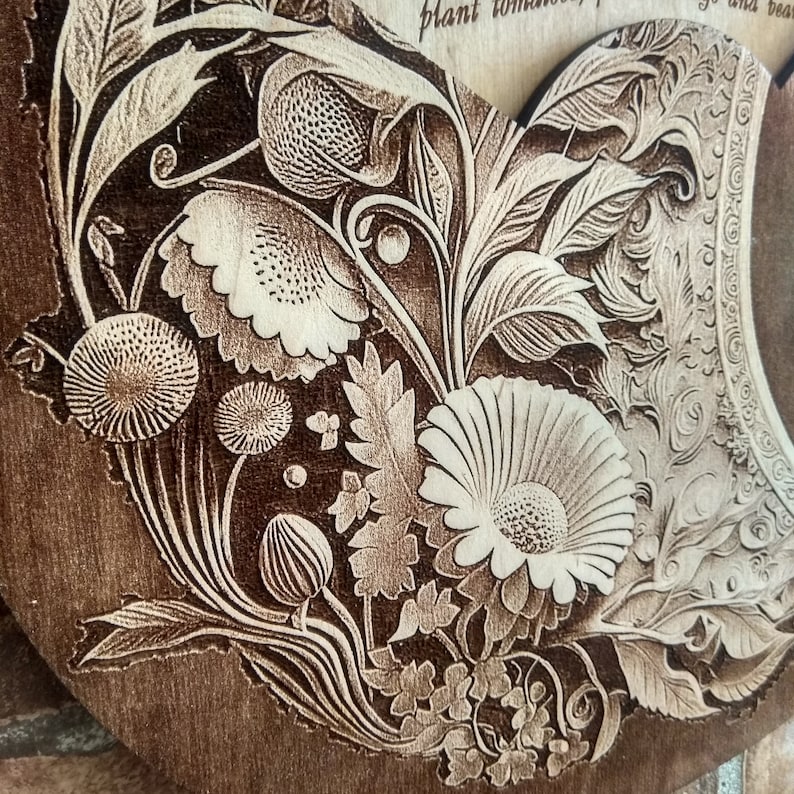 Peut inclure: Un gros plan d'une plaque en bois avec un motif floral d&eacute;taill&eacute; grav&eacute; &agrave; la surface. Le motif pr&eacute;sente une vari&eacute;t&eacute; de fleurs, de feuilles et de tiges, toutes finement grav&eacute;es dans une couleur brun clair sur un fond brun fonc&eacute;.
