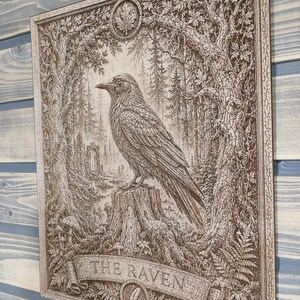 May include: A rectangular wooden wall plaque featuring a detailed laser-engraved illustration of a raven perched on a tree stump within a forest. The artwork includes an arched stone structure in the background and a banner at the bottom with the text THE RAVEN.
