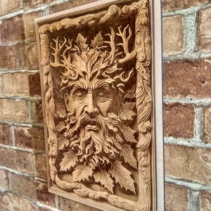 Puede incluir: Un adorno de pared de madera con una imagen tallada del Hombre Verde, una figura m&iacute;tica con una cara rodeada de hojas y ramas.