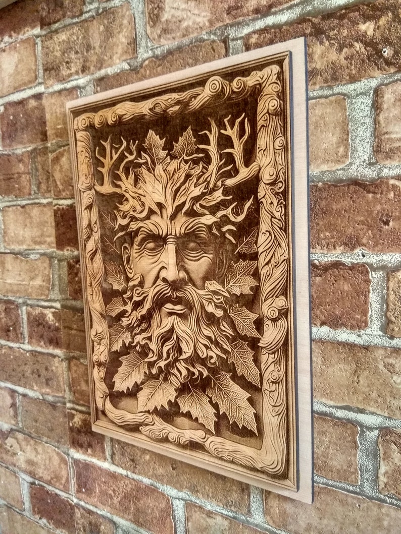 Puede incluir: Un adorno de pared de madera con una imagen tallada del Hombre Verde, una figura m&iacute;tica con una cara rodeada de hojas y ramas.