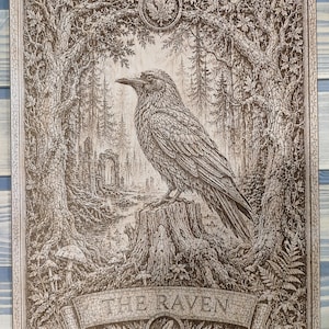 May include: A rectangular wooden wall art piece featuring a detailed brown-toned engraving of a raven perched on a tree stump. The scene includes a forest, stone ruins, and mushrooms. A banner at the bottom displays the text THE RAVEN with a feather icon.