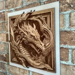 May include: A wooden wall art piece featuring a detailed carving of a dragon's head emerging from a frame. The dragon is carved in a 3D style, with its scales and wings appearing to come out of the wood.