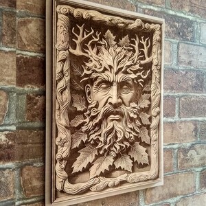 Puede incluir: Una pieza de arte de pared de madera con un dise&ntilde;o tallado de Green Man. La cara del Green Man est&aacute; rodeada de hojas y ramas, creando un motivo inspirado en la naturaleza.