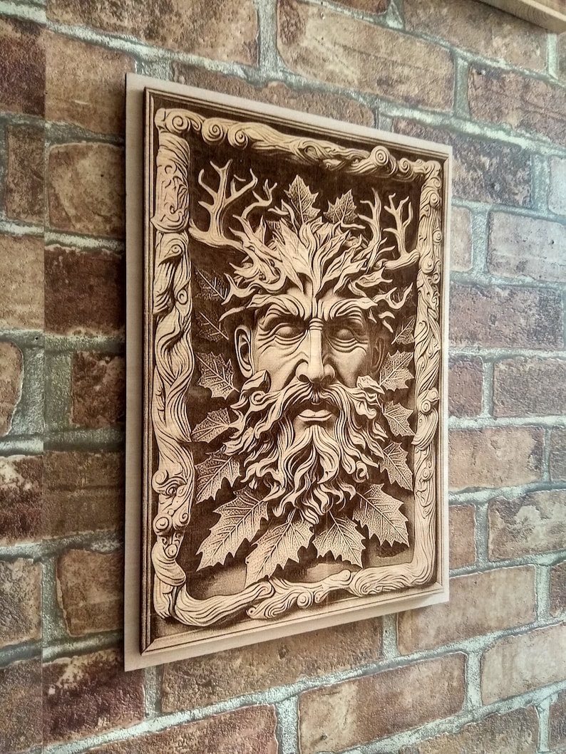Puede incluir: Una pieza de arte de pared de madera con un dise&ntilde;o tallado de Green Man. La cara del Green Man est&aacute; rodeada de hojas y ramas, creando un motivo inspirado en la naturaleza.