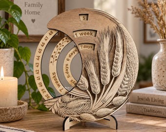 May include: A circular wooden pregnancy countdown calendar featuring laser-cut wheat stalks and leaves. The design includes rotating rings with numbers 38 through 48, weeks, and days, with cutouts displaying 1 week, 7 days, and the number 5.