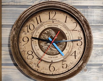 May include: A wooden clock with a distressed brown finish. The clock face features a wave design and the words "High Tide", "Low Tide", "Half Tide", and "Before High" and "After High". The clock hands are black, red, and blue.