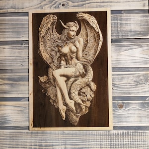 Op de afbeelding: Een gebrandschilderd beeld van een vrouw met hoorns en vleugels die op een draak zit. Het beeld is donkerbruin en heeft een gedetailleerd ontwerp.