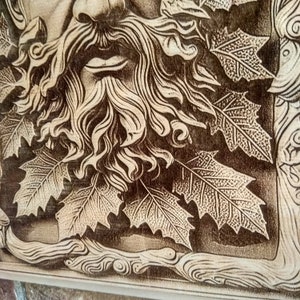 Puede incluir: Una talla de madera de una cara con barba y hojas que la rodean. La talla es de color marr&oacute;n claro y tiene un dise&ntilde;o detallado.