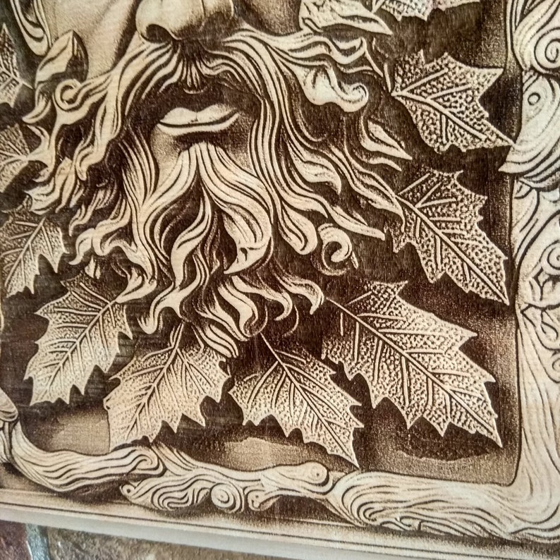 Puede incluir: Una talla de madera de una cara con barba y hojas que la rodean. La talla es de color marr&oacute;n claro y tiene un dise&ntilde;o detallado.