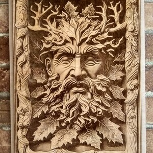Puede incluir: Una talla de madera de la cara de un hombre verde con barba y hojas que le crecen de la cabeza. La talla est&aacute; enmarcada en un marco de madera con un dise&ntilde;o tallado.