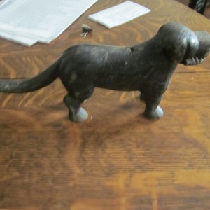 May include: A black cast iron dog doorstop with a long tail. The doorstop is on a wooden surface.