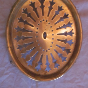 May include: A round, brass-colored metal tray with a decorative, cut-out design. The design features a circular pattern of radiating points.