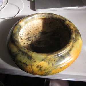 May include: A round, green, yellow, and brown stone bowl with a rough, textured surface.