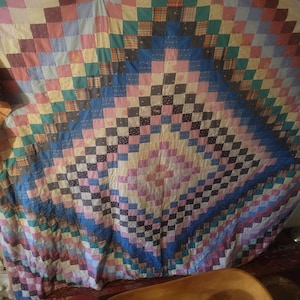 May include: A large, colorful quilt with a patchwork design. The quilt is made up of squares of different colors and patterns, including pink, blue, green, and yellow. The quilt is hanging on a wall.
