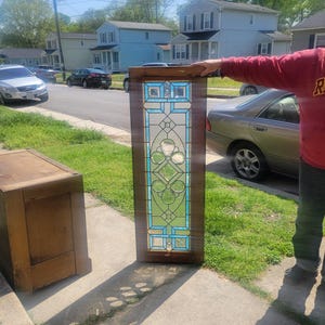 May include: A stained glass window panel with a geometric design featuring blue and clear glass. The panel is framed in wood and has a light brown finish.