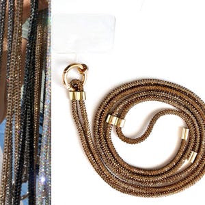 Może przedstawiać: Złoty naszyjnik z łańcuszkiem o błyszczącym, kryształowym wykończeniu. Łańcuszek składa się z wielu pasm i ma złote zapięcie.