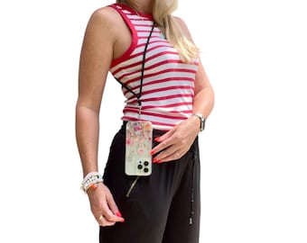 May include: A woman wearing a red and white striped tank top and black pants with a phone case attached to a black lanyard around her neck. The phone case has a floral design and a clear back.