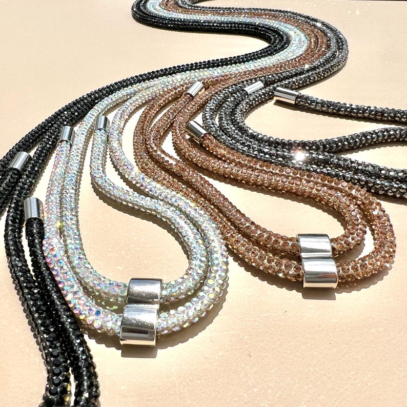 May include: A set of six multi-colored crystal necklaces with silver clasps. The necklaces are made of small, sparkling crystals and are arranged in a cascading pattern.
