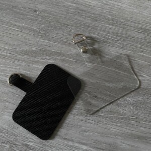 May include: A black fabric patch with a loop for attaching to a bag or other item. The patch is next to a clear plastic pocket with a metal ring and a snap closure.