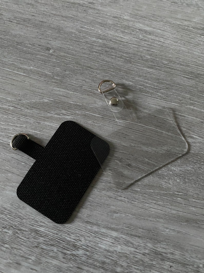 May include: A black fabric patch with a loop for attaching to a bag or other item. The patch is next to a clear plastic pocket with a metal ring and a snap closure.