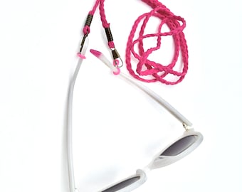 May include: White sunglasses with a pink braided cord. The sunglasses have a cat-eye shape and dark lenses.