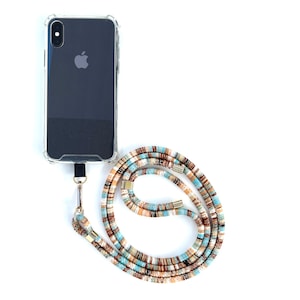 Puede incluir: Una funda de tel&eacute;fono negra con la parte posterior transparente y un cord&oacute;n para tel&eacute;fono con un patr&oacute;n de rayas azules, marrones y blancas.