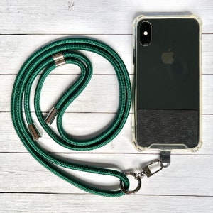 Może przedstawiać: Zielony pasek do telefonu z srebrnymi metalowymi klamrami i kółkiem. Pasek jest owinięty wokół przezroczystego etui na telefon z czarnym telefonem w środku.