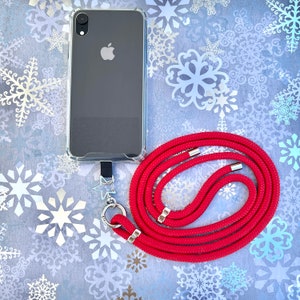 Może przedstawiać: Przezroczyste etui na telefon z czarnym telefonem w środku, przymocowane do czerwonego paska do telefonu z srebrnym zawieszką w kształcie gwiazdki.