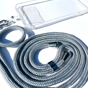 Może przedstawiać: Szary sznurek do telefonu z metalowymi klamrami w kolorze srebrnym. Sznurek jest zwinięty i gotowy do użycia. W zestawie znajduje się również przezroczyste etui na telefon.