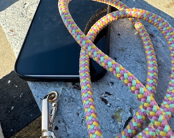 May include: A braided phone strap with a gold clasp. The strap is made of pink, yellow, and green braided cord.