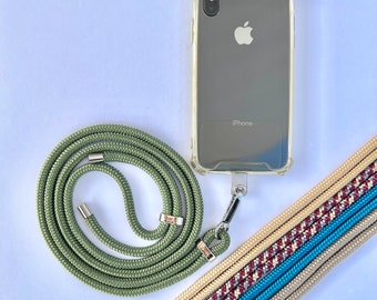 May include: A clear phone case with an iPhone inside, attached to a green rope lanyard with silver-colored metal hardware. Several multi-colored woven straps are also visible, offering alternative styles.