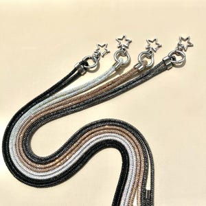 May include: Four phone straps with star-shaped charms. The straps are made of black, silver, and gold chain with rhinestones.