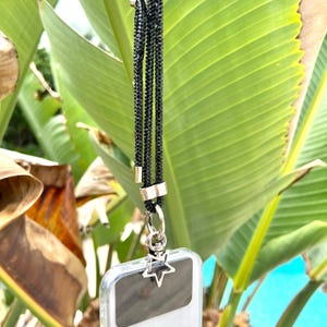 May include: A black phone strap with a silver star charm. The strap is made of a braided material and has a silver clasp.