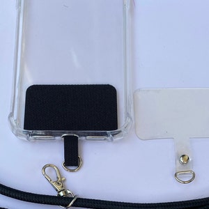 May include: A clear phone case with a black fabric patch on the back. The case has a black lanyard attached to it with a silver clip. A separate clear phone case with a silver clip is also shown.