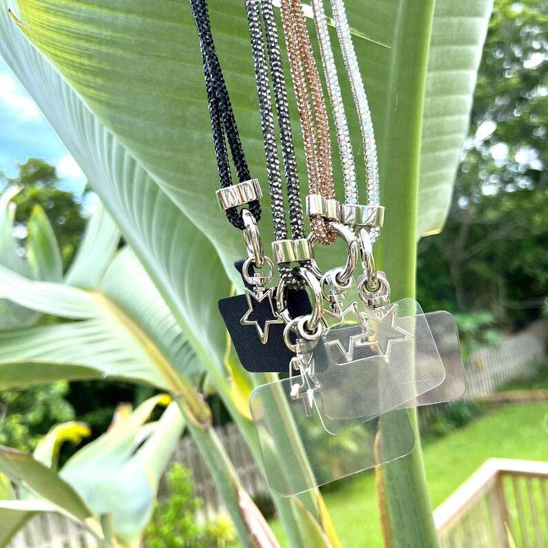 May include: Five different lanyards with star-shaped charms and clear plastic ID holders. The lanyards are made of black, gray, silver, and rose gold colored cords.