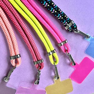 Może przedstawiać: Pięć kolorowych sznurków z srebrnymi klamrami i pasującymi plastikowymi uchwytami na identyfikatory. Sznurki są różowe, żółte, zielone, różowe i czarne w białe paski.