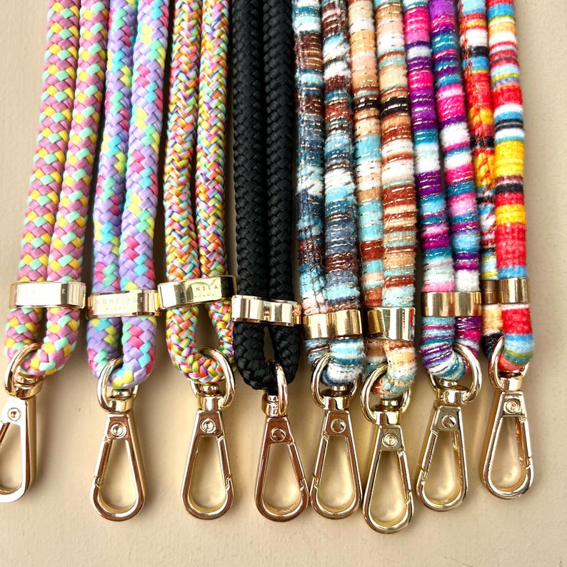 Puede incluir: Surtido de correas de cuerda coloridas y estampadas con cierres dorados. Las correas est&aacute;n hechas de diferentes materiales, incluyendo tejido tejido y cuerda trenzada.