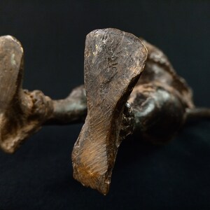 K&ouml;nnte beinhalten: Eine Bronzeskulptur einer liegenden Figur, von unten betrachtet. Die F&uuml;&szlig;e der Figur sind deutlich sichtbar, mit strukturierten Oberfl&auml;chen und einer dunklen, gealterten Patina. Die Skulptur ist vor einem dunklen Hintergrund platziert.