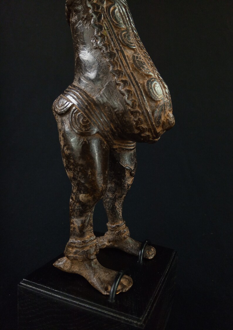 K&ouml;nnte beinhalten: Eine bronzefarbene Skulptur einer Figur mit detaillierten Schnitzereien. Die Figur hat einen runden Torso und Beine mit komplizierten Mustern am Oberk&ouml;rper. Die Skulptur ist auf einem schwarzen Sockel montiert.