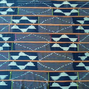 Peut inclure: Un tissu noir avec un motif géométrique blanc tissé dans le tissu. Le motif est composé de diamants et de triangles. Le tissu a une bande horizontale brune et orange qui traverse le tissu.