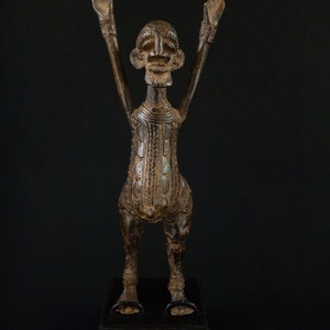 K&ouml;nnte beinhalten: Bronzefarbene Skulptur einer menschlichen Figur mit erhobenen Armen. Die Figur hat ein detailliertes Gesicht und einen Torso mit gemusterten Designs. Sie steht auf einem schwarzen rechteckigen Sockel.