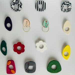 May include: A selection of colourful, handmade earrings in various shapes and designs. Includes floral, geometric, and abstract patterns. The earrings are in shades of red, green, yellow, white, and black.