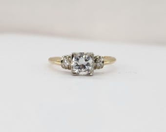 May include: A gold engagement ring with a single round diamond and two smaller diamonds on either side.