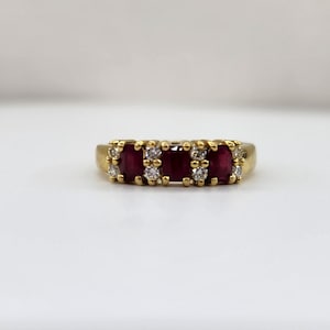 May include: A gold band ring with three red rubies and small diamonds set in the band.