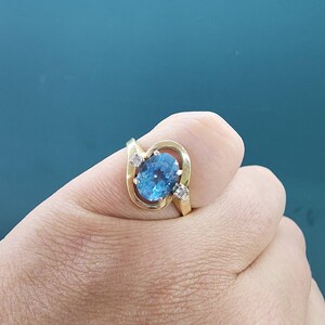 May include: A gold ring with a blue oval gemstone and two smaller diamonds. The ring is set in a twisted band.