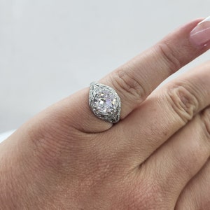 May include: A silver ring with a large, round, clear gemstone. The ring has an ornate filigree design around the gemstone and on the band. The ring is on a finger.