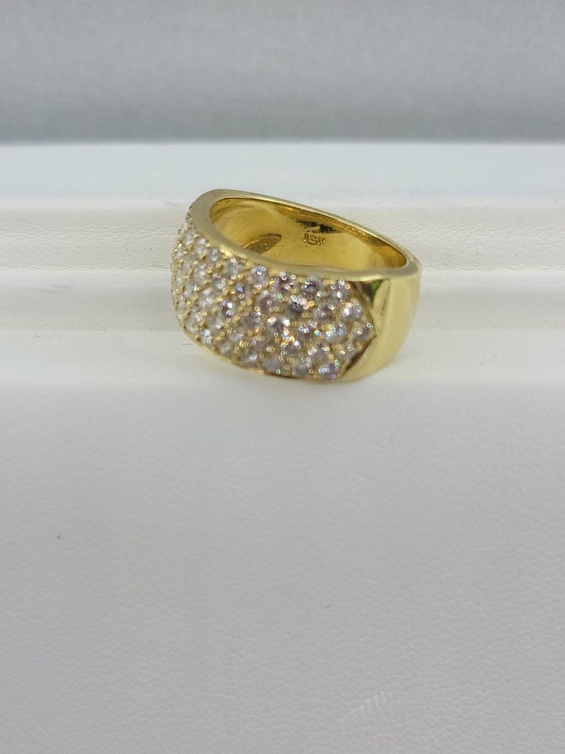 May include: A gold band ring with a wide, flat top that is completely covered in small, clear stones.