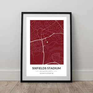 May include: Framed print showing a map of Sixfields Stadium, Northampton. The map is a deep red with white roads and a pin marking the stadium. The text "SIXFIELDS STADIUM" is at the bottom, along with coordinates.