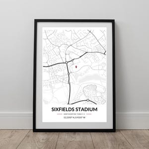May include: Framed print featuring a black and white map of the area around Sixfields Stadium, home to Northampton Town F.C. A red marker pinpoints the stadium's location. The print includes the stadium's name and coordinates, all within a black frame.