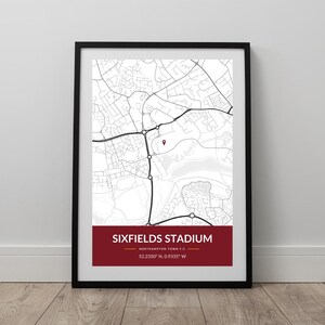 May include: Framed map print of Sixfields Stadium, Northampton, UK. The map is in monochrome, with a red marker indicating the stadium's location. The stadium's name and coordinates are displayed on a red banner at the bottom.